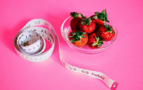 A glass bowl of fresh strawberries paired with a pink measuring tape symbolizes healthy eating.