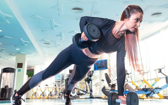 Woman performing a plank row with dumbbells in a bright Dubai gym.