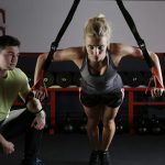 A woman performing strength training with a trainer in a gym setting, showcasing fitness and dedication.