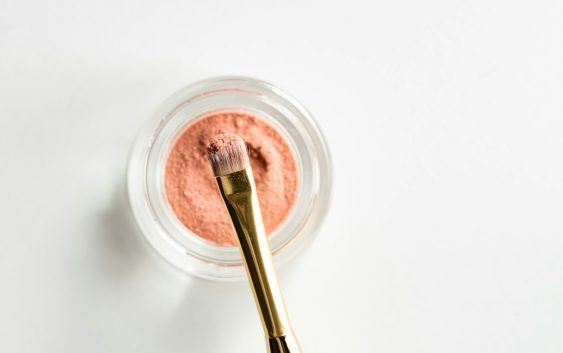 brown makeup brush in front pink powder on glass case